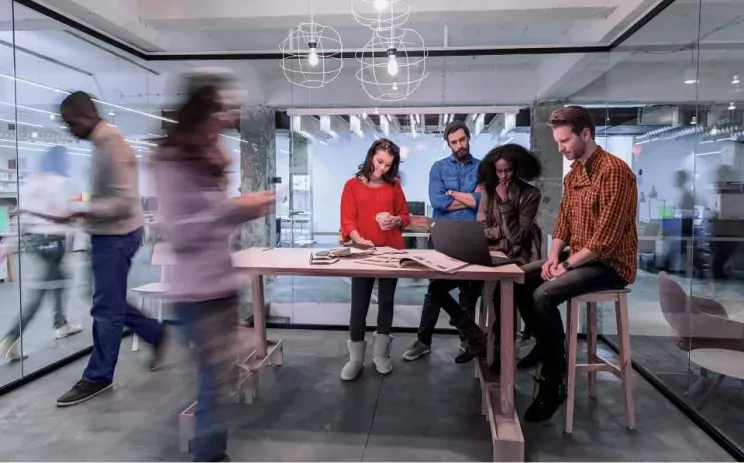 Several people are working on a laptop in the open space office